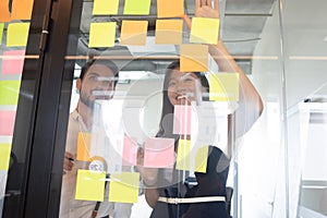 Smiling diverse employees looking at sticky papers on glass wall