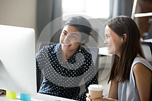 Smiling diverse female interns talking in office discussing onli photo