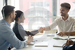 Smiling diverse partners handshake collaborating at office meeting