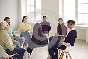 Smiling diverse people listening to young man sharing his story in a group therapy session