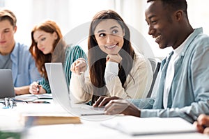 Smiling diverse students sitting at desk working on group project