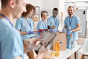 Smiling diverse volunteers sorting foodstuff in cardboard boxes, working together on donation project