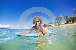 Smiling diverse young boy boarding in the beautiful blue ocean