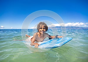 Smiling diverse young boy boarding in the beautiful blue ocean