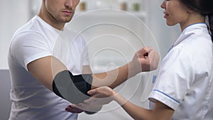 Smiling doctor fixing elbow padded orthosis pleased sportsman patient, rehab