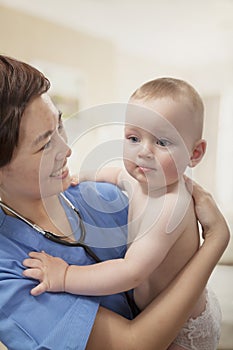 Smiling doctor holding baby in her arms in the doctors office