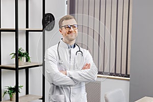 Smiling doctor posing with arms crossed in the office. Man is wearing a stethoscope and glasses. Medical staff on the workplace