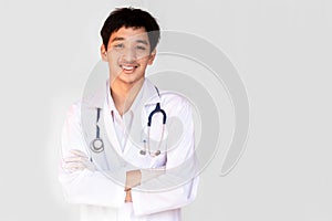 A smiling doctor posing with arms crossed on a white background is wearing a stethoscope. Young Asian doctor wearing a white coat