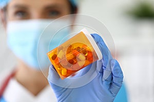 Smiling doctor in protective mask holds jar of pills.