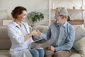 Smiling doctor and senior patient handshake during medical homecare visit