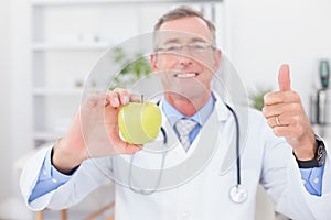 Smiling doctor showing apple with thumbs up