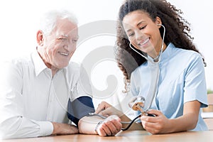 Smiling doctor with stethoscope examining happy elderly man in t