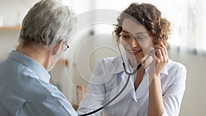 Smiling doctor using stethoscope, listening to mature patient heartbeat