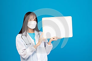 Smiling doctor wearing face mask holding blank banner or card with stethoscope on blue background