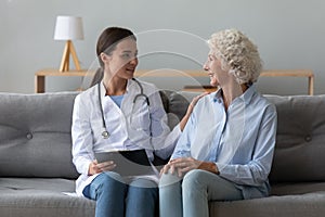 Smiling doctor consulting older woman patient during visit at home photo