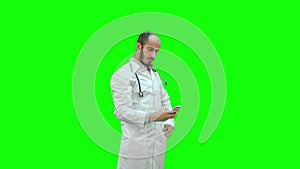 Smiling doctor in white coat with stethoscope taking selfie on his phone on a Green Screen, Chroma Key.