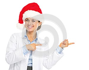 Smiling doctor woman in santa hat pointing on copy space