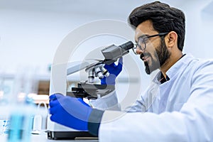 Smiling doctor working in modern laboratory research scientist examines substance under microscope.