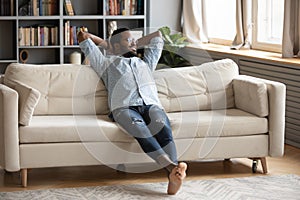 Smiling dreamy African American man sitting on cozy couch