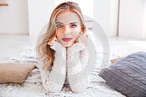 Smiling dreamy girl in sweater lying on floor and relaxing