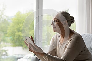 Smiling dreamy middle aged woman in glasses using cellphone.