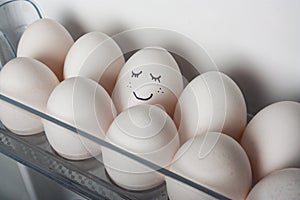 Smiling egg in a row of white eggs in fridge