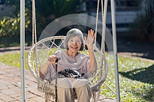 Smiling elderly asian woman wave to camera on swing