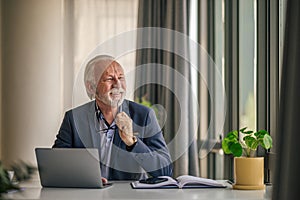 Smiling elderly businessman with laptop looking away at desk in office