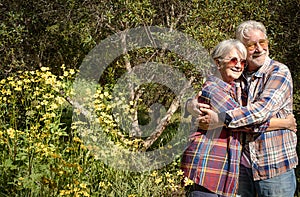 Smiling elderly couple in the forest hugging each other enjoying the spring and flowering. Two retirees who love a healthy