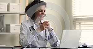 Smiling elderly female family therapist in headphones support patient online