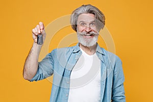 Smiling elderly gray-haired mustache bearded man in casual blue shirt posing isolated on yellow wall background studio