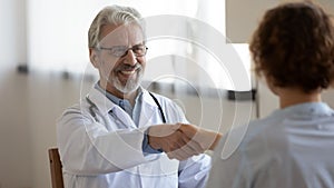 Smiling elderly male doctor handshake patient at consultation