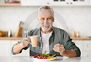 Smiling elderly man eating lunch and enjoying cup of coffee