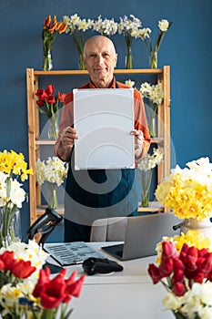 Smiling elderly man European florist holds a white board in his hands.