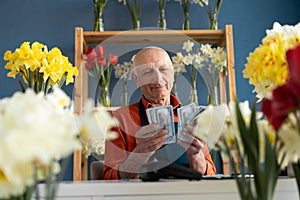 Smiling elderly man flower seller of European appearance holds dollars in his hands