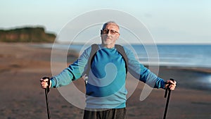 Smiling elderly man grandfather posing with Scandinavian walking stick at sea beach sunset closeup