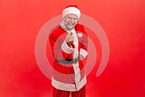 Smiling elderly man with gray beard wearing santa claus costume gesturing come to me, beckoning with