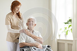 Smiling elderly man in a wheelchair and friendly caregiver in a