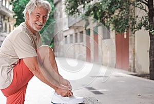 Smiling elderly man with white hair ties his shoelaces on a city tour. Senior retired enjoying fitness and walking