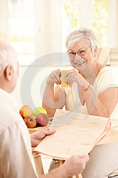 Smiling elderly wife sitting at table with mug