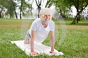 smiling elderly woman doing plank on yoga mat