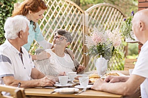 Smiling elderly woman eating breakfast with friends and her care