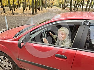 The smiling elderly woman in a red jacket at the wheel of the car