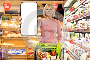 Smiling elderly woman shopping at supermarket, showing smartphone, mockup