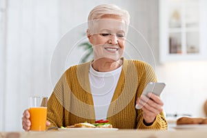 Smiling elderly woman using mobile phone while having lunch, closeup