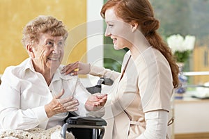 Smiling elderly woman talking with friendly caregiver in the nursing house