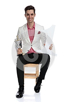 Smiling elegant champion sitting and holding his prizes