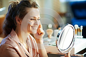 Smiling elegant woman applying cream and looking in mirror