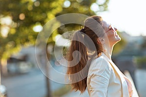 smiling elegant woman in pink dress and white jacket in city