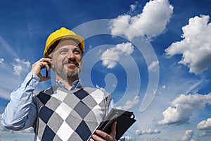 Smiling Engineer Talking On Mobile Phone Against Blue Sky With White Clouds